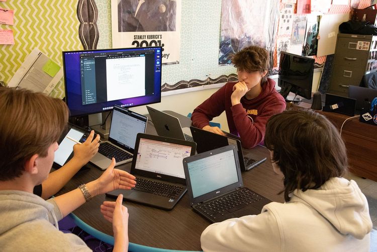 Students sitting around laptops having a discussion.