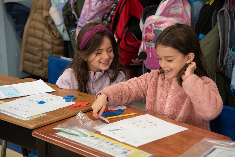 Two elementary students using the math manipulatives at their desks.