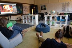 A classroom with bean bag chairs and a whiteboard playing a fireplace scene with students relaxing and reading.