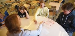 Students and teacher working on math problems on a whiteboard activity table.