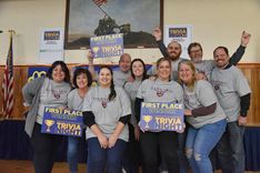 A group of people in grey matching shirts holding First Place winner signs at CFEE Trivia Night.